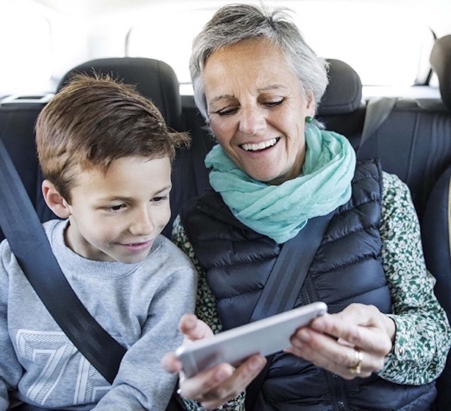 Photo of smiling silver-haired woman sharing mobile device images with a young boy